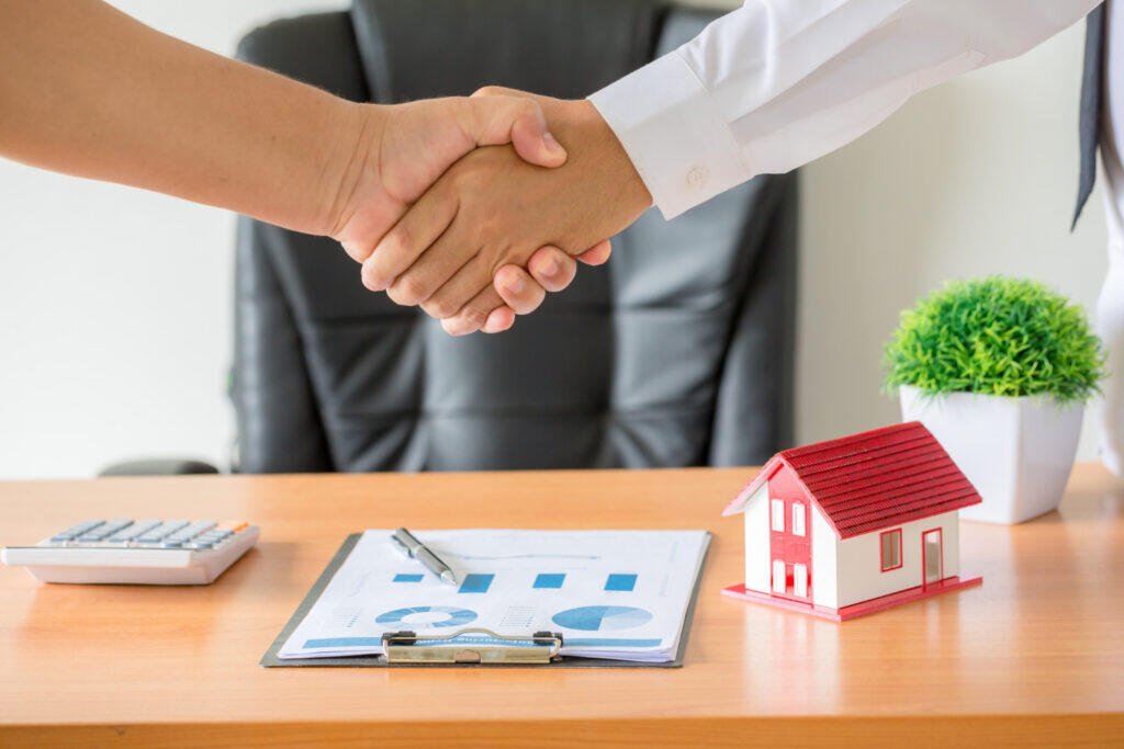 Business handshake over real estate investment documents and house model. Adelaide real estate coaching.