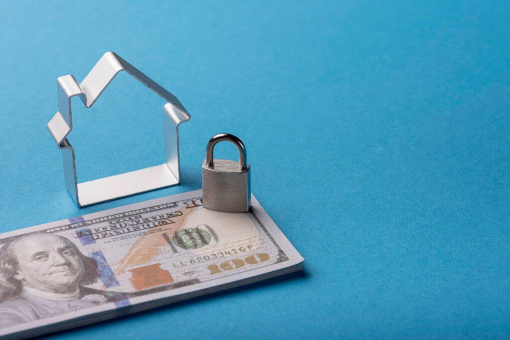 House-shaped cookie cutter, padlock, and US $100 bills. Wealth protection concept.
