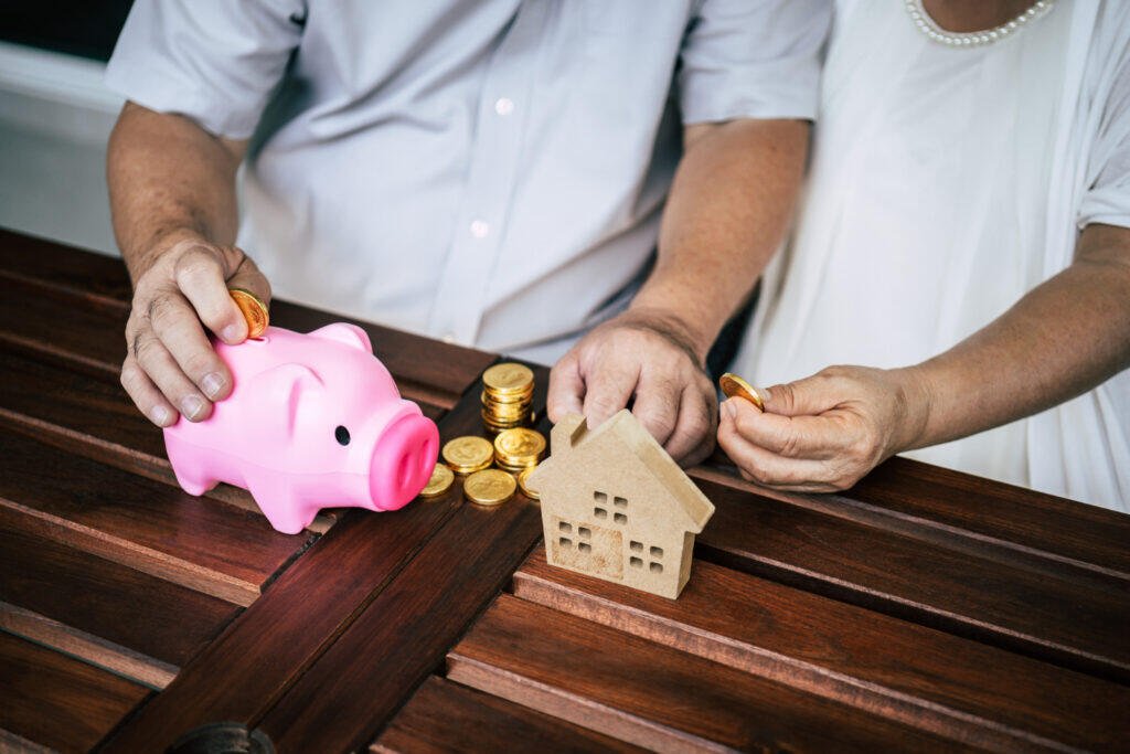 Senior couple saving for retirement in Adelaide, placing coins in piggy bank and beside a house model.