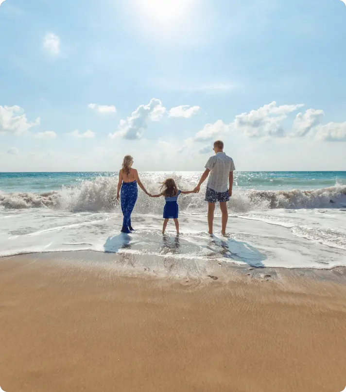 Family holding hands on a beach, enjoying a sunny day.